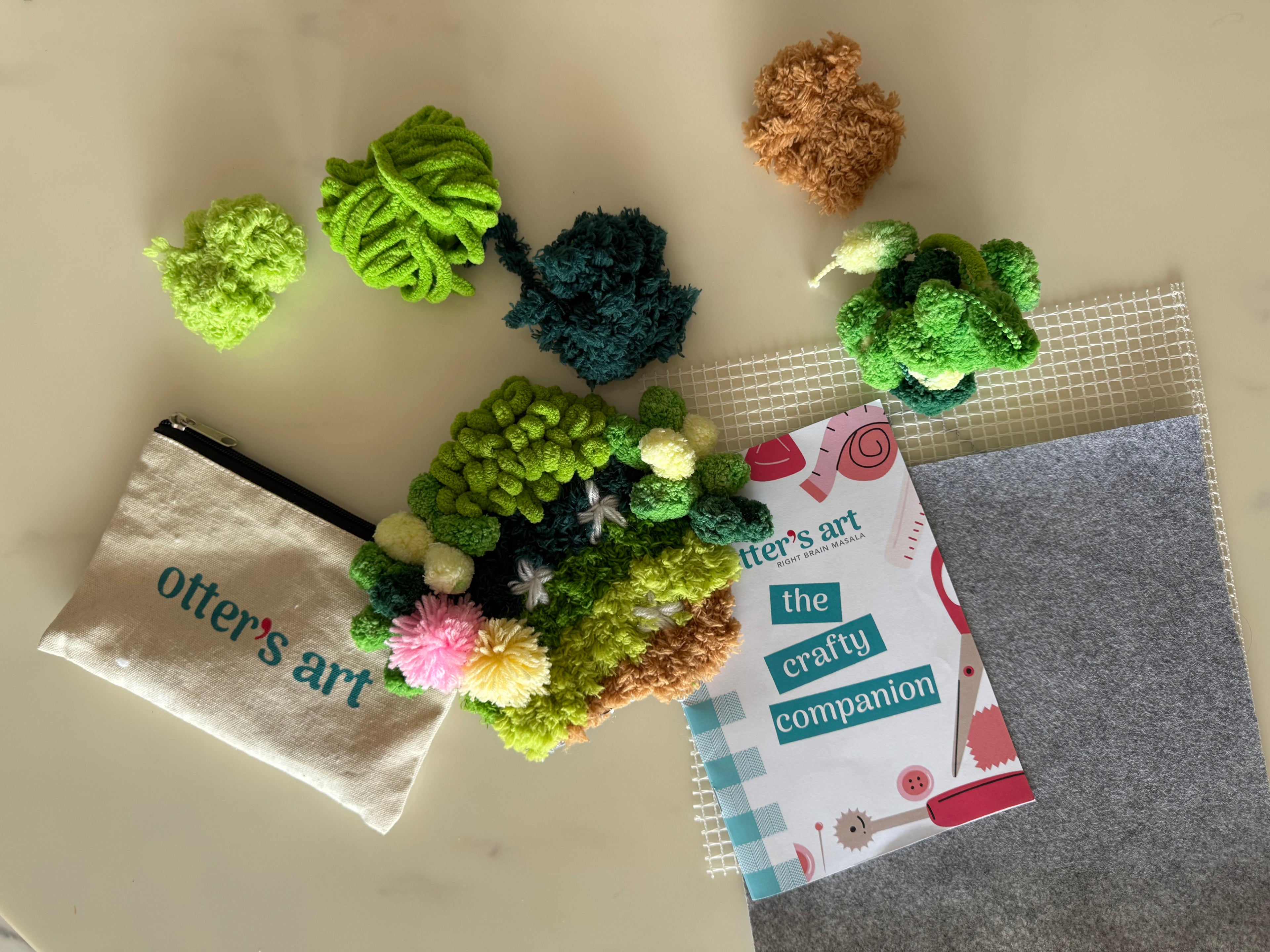 Craft materials including a pouch, book, and various textured green and brown shapes on a light surface.