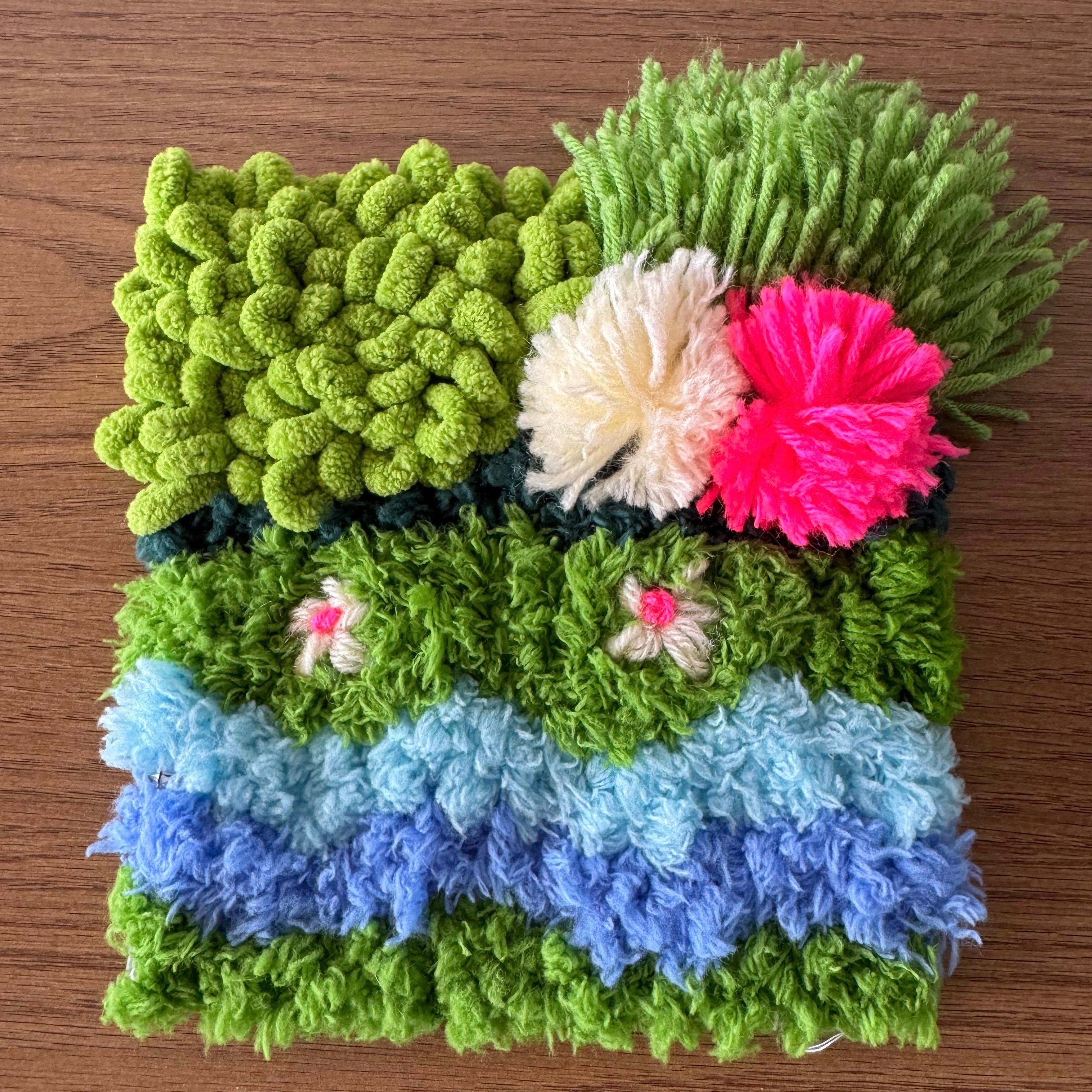 Deep greens, misty blues, and a splash of neon pink and cream, Monsoon Magic captures that first-rain feeling, when everything turns lush and a little wild. Textured loops mimic overgrown moss, dotted with tiny embroidered flowers and playful pom-poms for a coaster that feels like a rain-soaked garden caught mid-bloom.