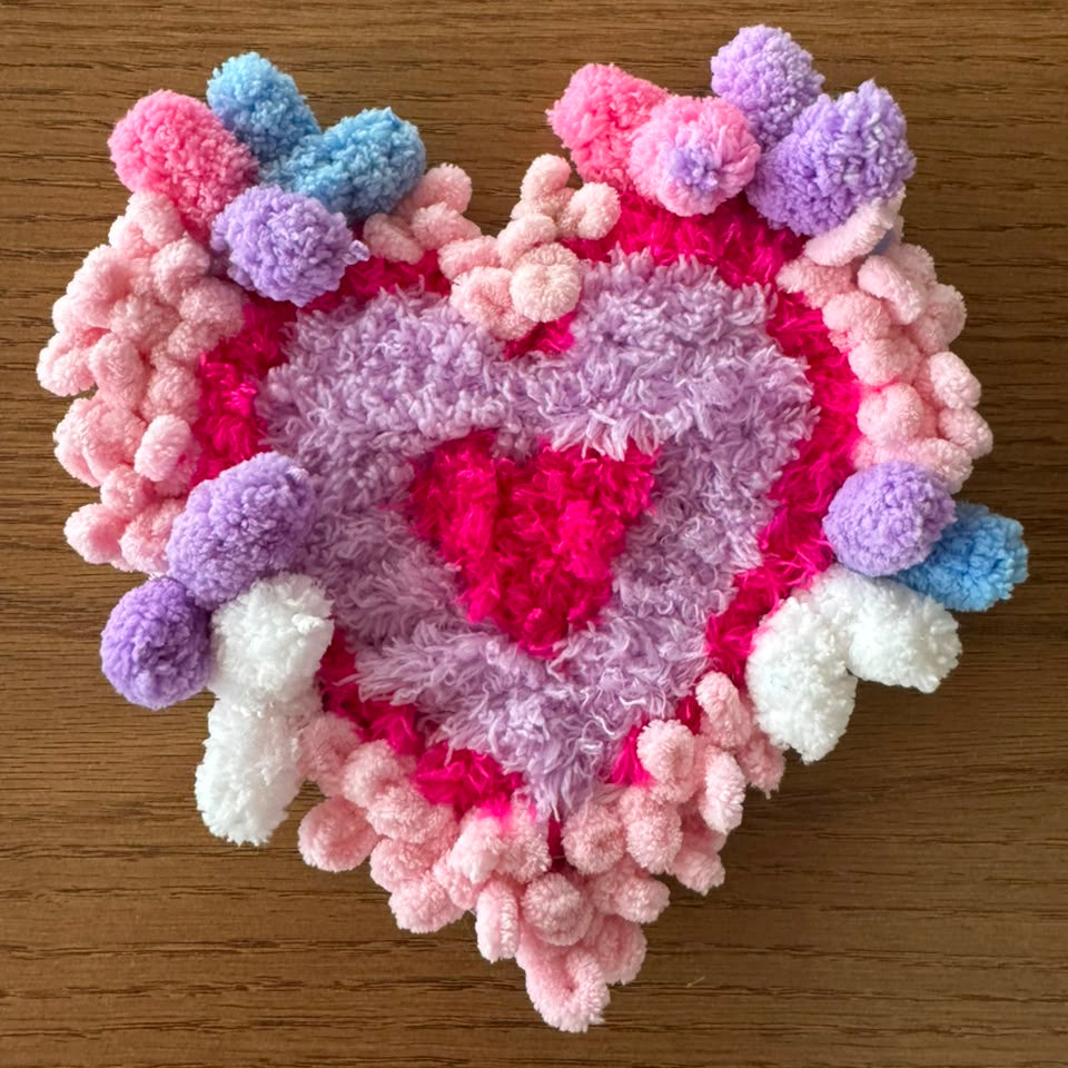 A heart within a heart — Sweetheart layers hot pink, lilac, and blush into a soft, romantic coaster, framed with cloud-like pom-poms in baby blue, lavender, and white. Equal parts sweet and playful, it's the one made for anyone who wants their coaster collection to feel like a love letter.