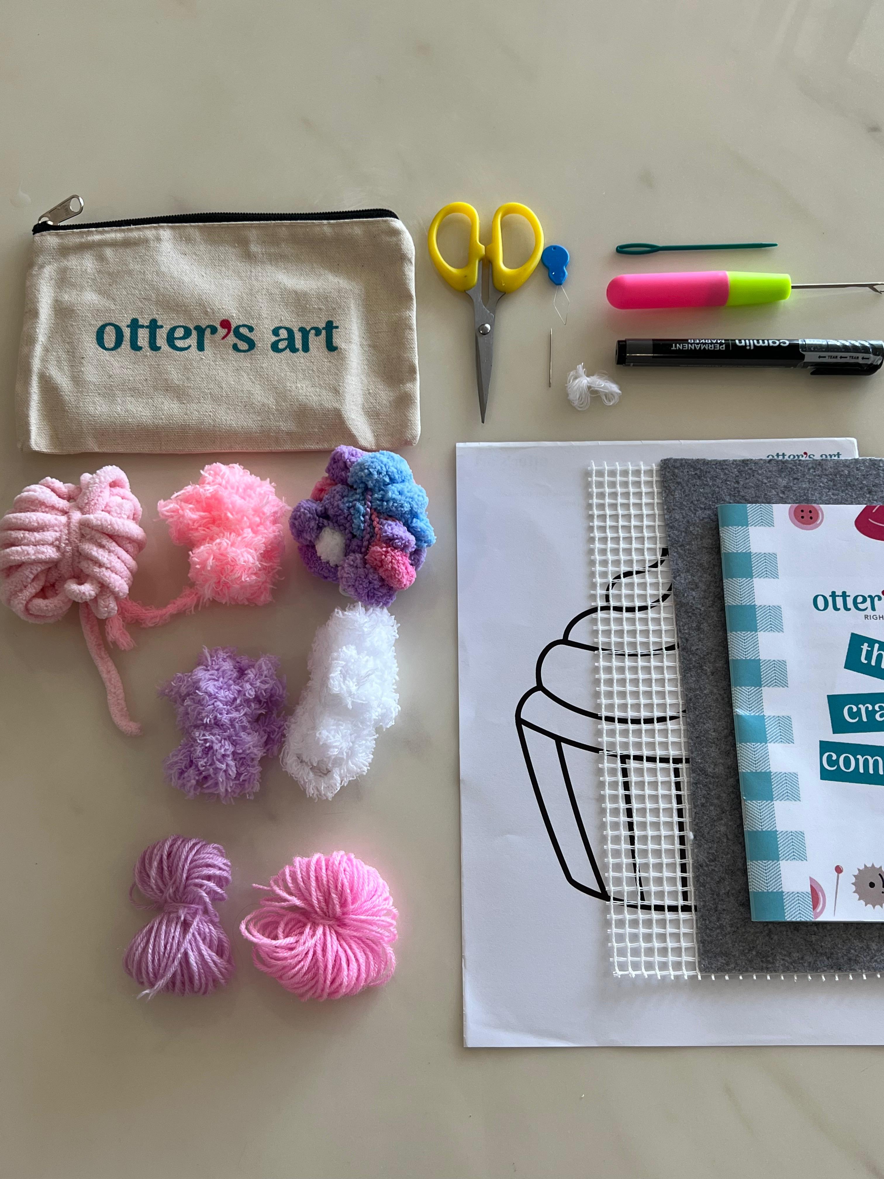 Unicorn Cupcake DIY moss coaster kit with pastel yarn colors. Crafting supplies including yarn, scissors, and a pouch labeled 'otter's art' on a light surface for a DIY Kit